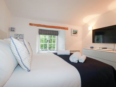 A bedroom with a bed with pillows and rolled towels near a window and a television at 2 Rose Cottage in St Agnes