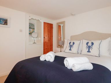 A bedroom with a bed with lobster printed pillows white towels on a navy bedspread a wooden door and a mirror at 2 Rose Cottage in St Agnes