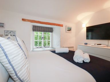 A bedroom with a bed towels and television on a dresser at 2 Rose Cottage in St Agnes