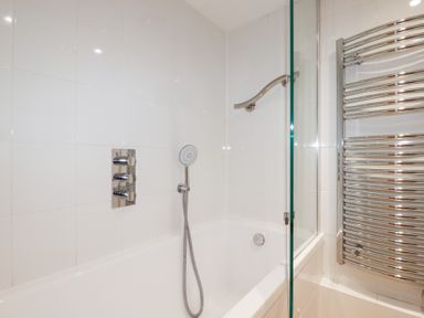 A bathroom with a bathtub shower and a chrome towel radiator at 2 Rose Cottage in St Agnes