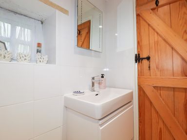 A bathroom sink with a faucet and soap dispenser next to a wooden door and window at 2 Rose Cottage in St Agnes