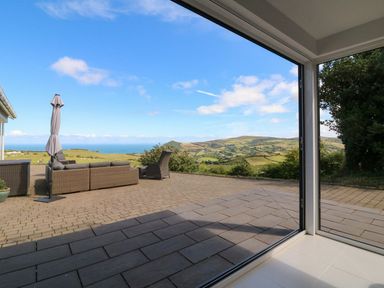 An outdoor patio with wicker furniture and umbrella overlooking green hills and sea at Buddicombe House Combe Martin
