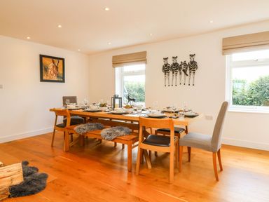A dining room with a wooden table set for eight people and two windows at Buddicombe House in Combe Martin