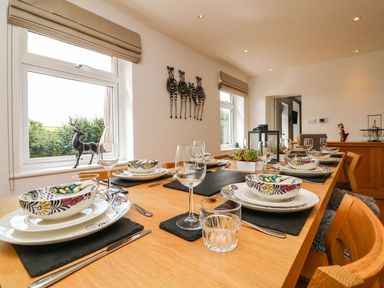A dining room with a wooden table set with plates bowls glasses and cutlery at Buddicombe House in Combe Martin