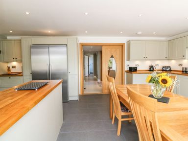 A kitchen with wooden dining table and chairs a vase with flowers stainless steel fridge and light-colored cabinets at Buddicombe House in Combe Martin