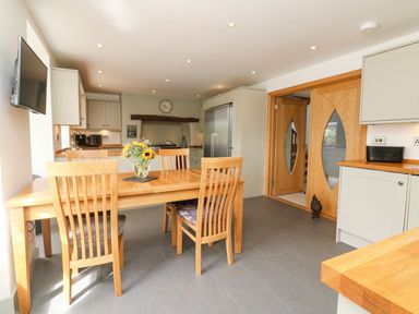 A kitchen with wooden dining table and chairs a wall-mounted television and a large refrigerator at Buddicombe House in Combe Martin