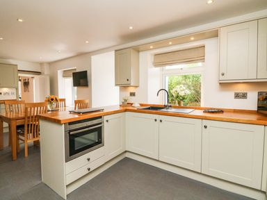 A kitchen with wooden countertops cabinets an oven a sink and a dining table with chairs at Buddicombe House in Combe Martin