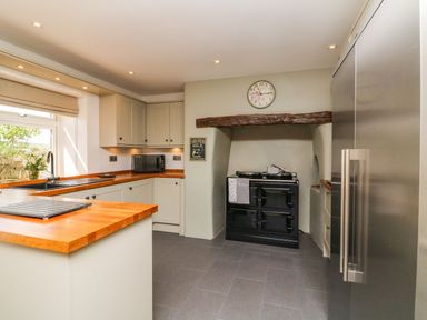 A kitchen with wooden countertops a black stove under a wooden beam a microwave and a stainless steel refrigerator at Buddicombe House in Combe Martin