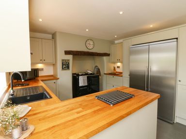 A kitchen with wooden countertops a black sink a large silver refrigerator and a stove under a wooden beam at Buddicombe House in Combe Martin