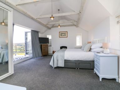 A bedroom with a bed bedside tables a television and a glass door leading to a balcony at Buddicombe House in Combe Martin