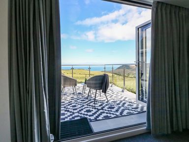 A balcony with two chairs and a table overlooking fields and the sea at Buddicombe House in Combe Martin