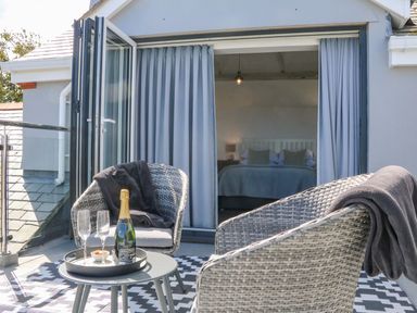 A balcony with two wicker chairs a small table with a bottle of champagne and glasses and an open door leading to a bedroom at Buddicombe House in Combe Martin