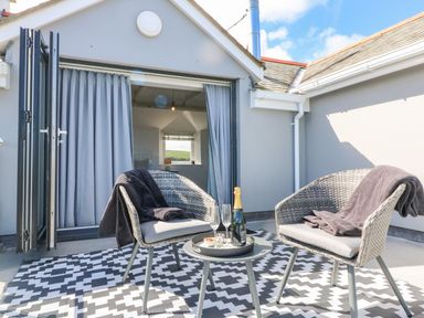 A patio with two wicker chairs and a small round table with a bottle and glasses outside an open door at Buddicombe House in Combe Martin