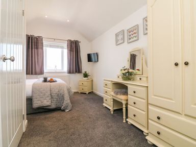 A bedroom with a bed window curtains a wall-mounted television a dressing table with a mirror and a wardrobe at Buddicombe House in Combe Martin