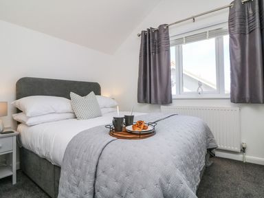A bedroom with a bed with grey headboard and bedding next to a window with grey curtains at Buddicombe House in Combe Martin