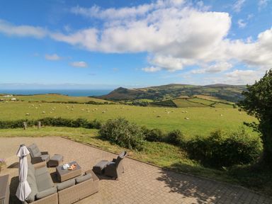 An outdoor patio with wicker furniture overlooking green fields with sheep and hills at Buddicombe House in Combe Martin