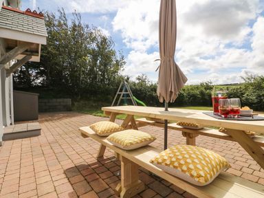 An outdoor patio area with a wooden picnic table and benches with yellow patterned cushions and an umbrella at Buddicombe House in Combe Martin