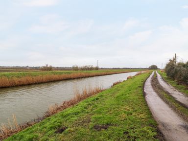 A dirt road next to a canal with grassy banks and fields in the background at Cuckoo in Ramsey Huntingdon