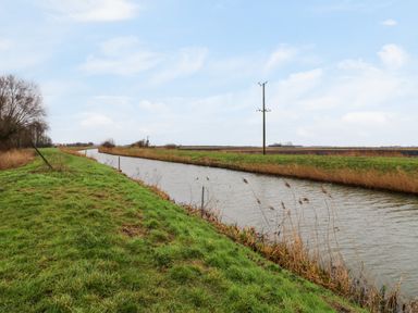 A canal with grassy banks and telephone poles in a rural area at Cuckoo in Ramsey Huntingdon