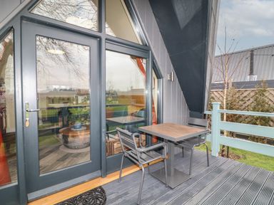 A small outdoor balcony with a table and two chairs in front of glass doors at Sunflower Lodge Near Misterton