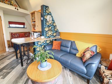 A living room with a blue sofa orange cushions floral wall clock and a wooden table at Sunflower Lodge Near Misterton