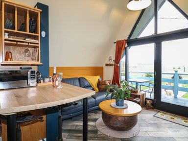 A living room with a wooden table a blue sofa a round coffee table with a plant and large windows with orange curtains at Sunflower Lodge Near Misterton