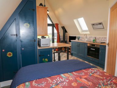 A small kitchen with blue cabinets a stove oven microwave and a dining counter next to a bed at Sunflower Lodge Near Misterton