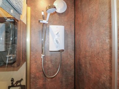 A shower with a white electric shower unit and handheld showerhead at Sunflower Lodge near Misterton