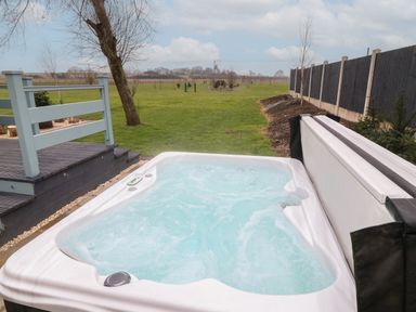 An outdoor jacuzzi with bubbling water next to a wooden deck and green lawn at Sunflower Lodge Near Misterton