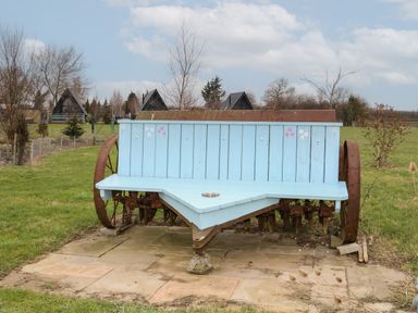 A light blue wooden bench with flower decorations placed on an old rusted farm machine in a grassy outdoor area at Sunflower Lodge Near Misterton