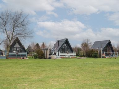 Three a frame cabins with fenced patios on a large grassy field with trees in the background at Sunflower Lodge Near Misterton