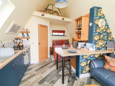 A kitchen with blue cabinets and wooden countertop next to a dining area with bar stools and a decorated wall near a bed in a small room at Sunflower Lodge Near Misterton