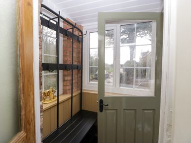 An entryway with a green door and black coat rack bench next to brick wall and windows at Court House Cottage in Gatcombe near Blakeney