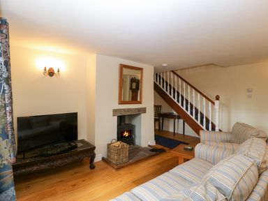 A living room with a striped sofa a wood burning stove a wicker basket a television on a wooden table and stairs at Court House Cottage in Gatcombe near Blakeney