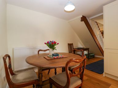 A dining area with a round wooden table and four chairs with flowers on the table at Court House Cottage in Gatcombe near Blakeney
