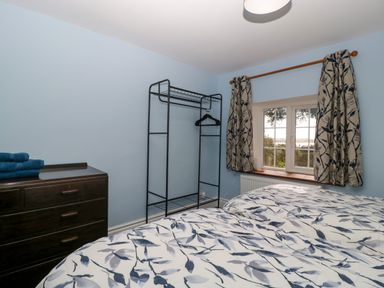 A bedroom with twin beds featuring patterned bedding a dark dresser with folded towels an open clothes rack and a window with patterned curtains at Court House Cottage in Gatcombe near Blakeney
