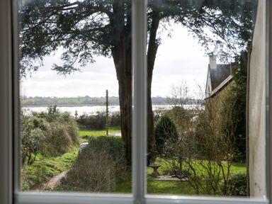 A garden with trees bushes and grass seen through a window at Court House Cottage Gatcombe near Blakeney