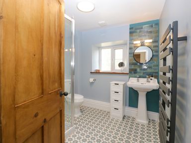 A bathroom with a wooden door patterned floor a pedestal sink mirror towel radiator and a window at Court House Cottage Gatcombe near Blakeney