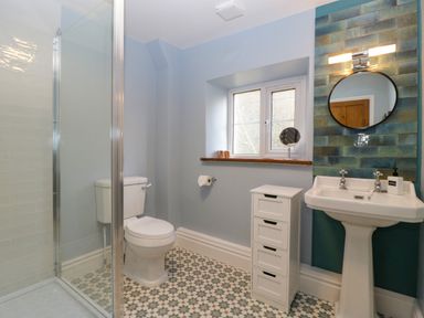 A bathroom with a toilet shower pedestal sink round mirror and small white storage unit at Court House Cottage Gatcombe near Blakeney