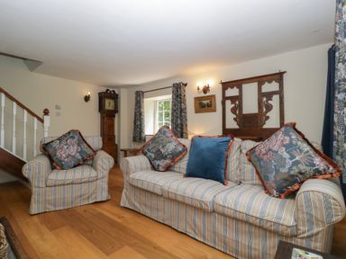 A living room with a sofa, armchair, and wall clock at Court House Cottage in Gatcombe near Blakeney