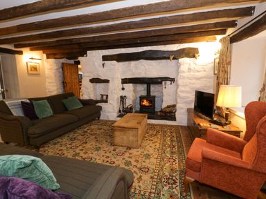 A living room with sofas and armchair around a fireplace with wooden beams on the ceiling at Glandwr Cottage in Llanbedr