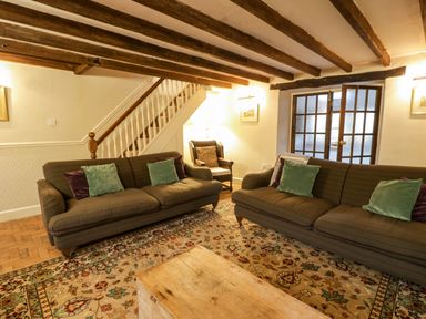 A living room with two sofas a wooden coffee table an armchair and stairs at Glandwr Cottage in Llanbedr