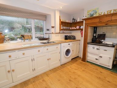 A kitchen with white cabinets a washing machine a sink a toaster and an old stove at Glandwr Cottage in Llanbedr