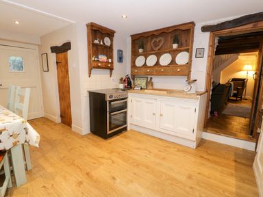 A kitchen with wooden floor a stove white cabinets and wooden shelves with plates at Glandwr Cottage in Llanbedr
