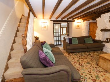 A living room with two sofas and a patterned rug near a staircase and wooden beams at Glandwr Cottage in Llanbedr