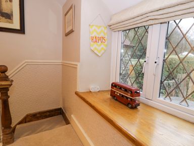 A staircase landing with a wooden banister and a wooden windowsill with a model red double-decker bus and a yellow and white decorative hanging at Glandwr Cottage in Llanbedr