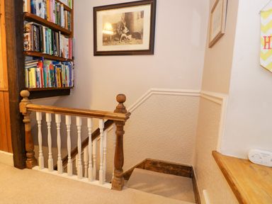 A staircase with wooden banister and bookshelf full of books on the wall at Glandwr Cottage in Llanbedr