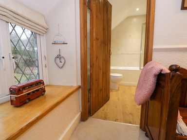 A wooden door open to a bathroom with a toilet and bathtub a window with a red toy bus on the sill and a heart decoration on the wall at Glandwr Cottage in Llanbedr