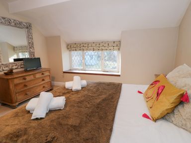 A bedroom with a bed covered with a brown blanket and white towels on top a wooden dresser with a mirror and small television in the corner at Glandwr Cottage in Llanbedr