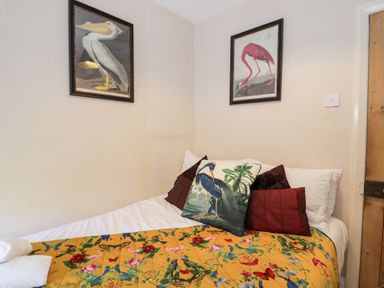 A bed with colorful bird and flower blanket and bird-themed pillows below two framed bird pictures at Glandwr Cottage in Llanbedr